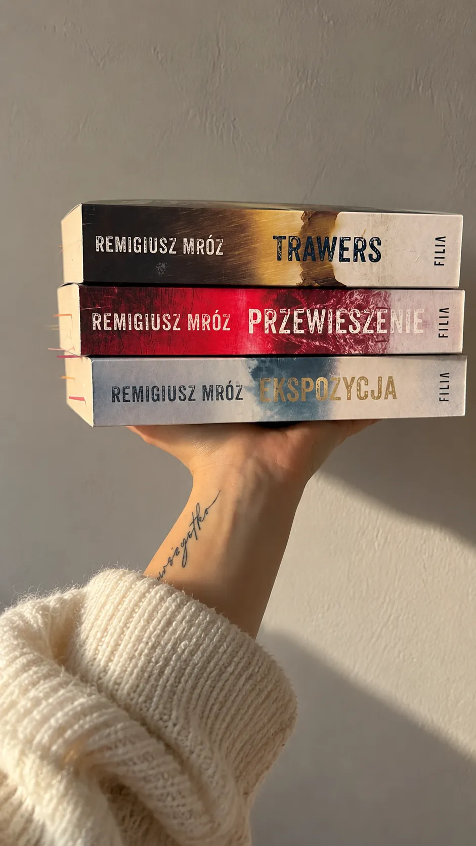 Dłoń trzymająca trzy kryminały Remigiusza Mroza: Trawers, Przewieszenie i Ekspozycja